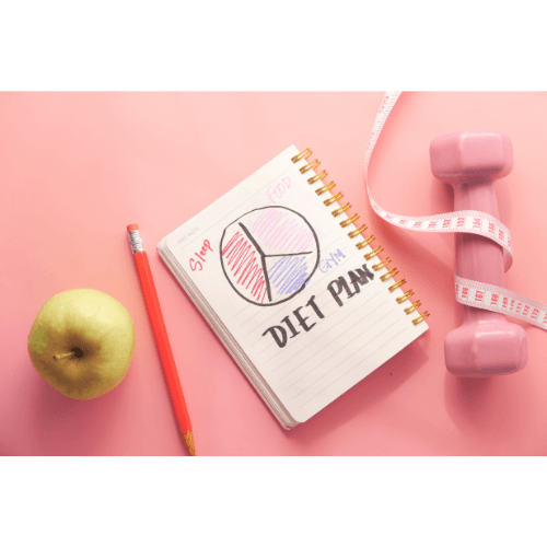 une pomme un stylo et un carnet, une altère et un mètre ruban posés sur fond rose